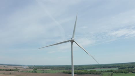 Spinning-windmill-blades-against-pale-blue-sky-with-soft-thin-clouds-seen-from-drone-orbiting