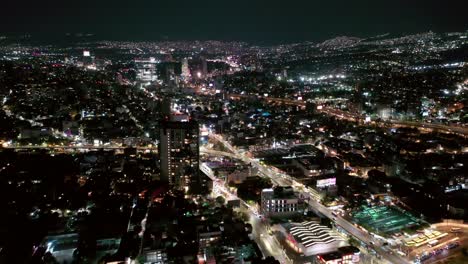 Flying-over-Mexico-City-lit-up-at-night-with-Mixcoac-downtown-cityscape-skyline,-Aerial