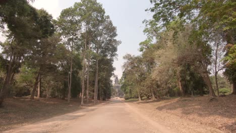 Road-surrounded-by-trees-leading-to-Angkor-Wat,-Siem-Reap,-Cambodia,-Dolly-in-shot