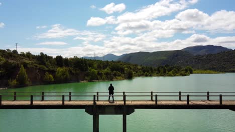 Aerial-view-of-a-man-standing-in-the-bridge,-over-the-green-lake