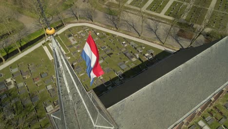 Niederländische-Nationalflagge,-Die-Auf-Einer-Stange-Weht,-Die-Am-Kirchturm-Befestigt-Ist,-Grabsteine