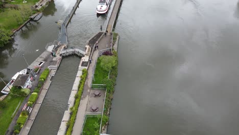 Marsh-Lock-near-Henley-on-Thames-large-boat-moving-out-of-lock-along-river-aerial-footage