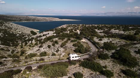 Cinematic-drone-movement-to-left-follow-a-van-driving,-showing-the-wonders-of-Croatia-in-its-mountains-and-accompanied-by-the-Adriatic-Sea-on-a-beautiful-sunny-day