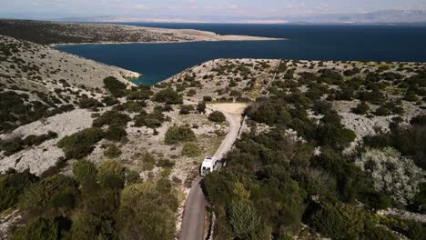 Aerial-shot-flying-over-a-road-surrounded-by-vegetation-and-rocks-following-a-white-truck-bound-for-the-Adriatic-Sea-off-the-coast-of-Croatia-Koromacno