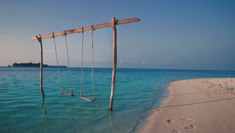 Cinemagraph-seamless-video-loop-of-a-wooden-swing-on-a-tropical-remote-dream-honeymoon-beach-at-the-seaside-on-an-empty-natural-adventure-island-in-Indonesia-with-white-sand-by-sunset