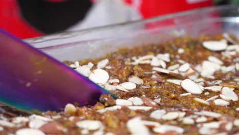 Slicing-a-piece-of-a-dry-fruit-dessert-cake-with-nut-shavings-and-a-large-purple-knife