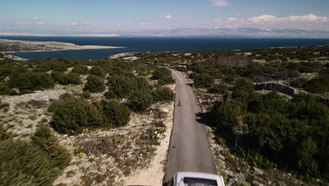 Low-altitude-straight-shot-with-drone-flying-over-a-van-driving-to-the-beach-on-a-road-surrounded-by-nature,-Croatia