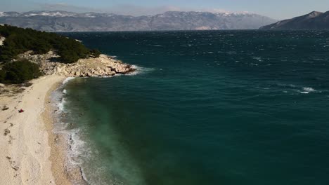 Aerial-plane-of-drone-with-panning-to-the-right-showing-the-beach-of-Baska-in-Croatia-in-the-Adriatic-Sea-on-a-beautiful-day-on-the-horizon-you-can-see-the-great-mountains-that-surround-it