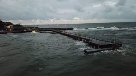 Drone-aerial-over-ocean-Melbourne-wavy-windy-cloudy-people-walking-on-pier