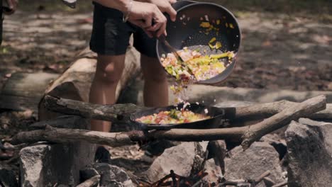 Adding-Vegetables-Into-A-Cast-Iron-Pan-Under-A-Campfire-in-Pulau-Ubin,-Singapore---close-up