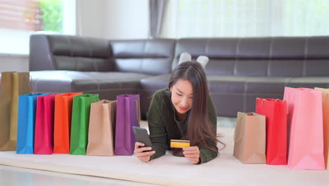 Rich-Asian-woman-surrounded-with-shopping-bags-typed-in-the-credit-card-number-to-pay-online