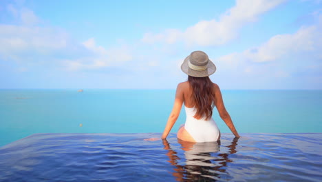 Beautiful-woman-sitting-at-infinity-pool-border-overlooking-the-ocean