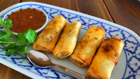 Rollitos-De-Primavera-Tradicionales-Con-Salsa-De-Chili-Dulce-En-Un-Plato-Blanco-Y-Azul-En-Un-Restaurante-Tailandés,-Tiro-En-Movimiento-De-4k