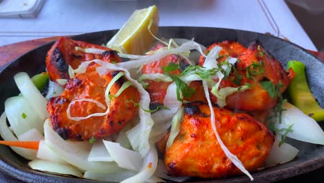 Traditional-Indian-Tandoori-chicken-with-onions-on-a-very-hot-plate-with-steam-smoke-in-a-restaurant,-4K-static-shot
