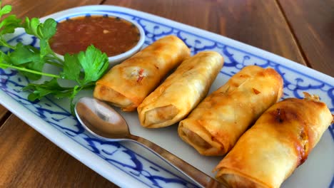 Traditional-spring-rolls-with-sweet-chili-sauce-on-a-white-and-blue-plate-in-a-thai-restaurant,-4K-moving-up-shot