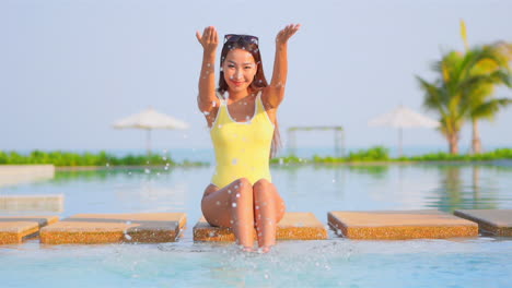 A-happy-playful-young-woman-splashes-pool-water-into-the-air