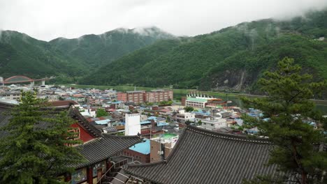 Panning-on-Danyang-city-panorama-prom-high-point,-Korean-traditional-temple-building-in-foreground-against-Mountains-in-a-haze-after-rain
