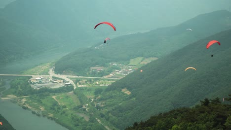 Paragliders-descending-between-the-mountains-in-Danyang-South-Korea,-city-over-view-from-top-aerial-point