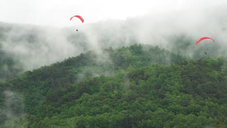 Two-paragliders-slowly-descending-over-the-mountain-which-vaporizing-after-the-rain