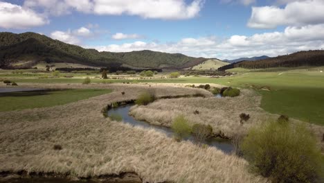 Winding-creek-in-natural-valley,-meandering-river-through-grass-land