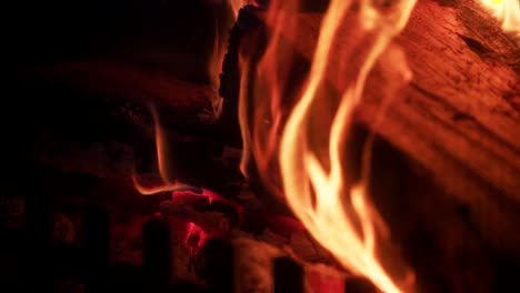 Glowing-hot-flames-on-side-of-wooden-log-in-fireplace,-orange-heat