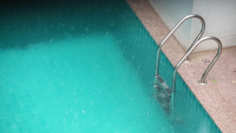 Close-up-of-swimming-pool-with-ladder-with-rain-falling-heavily-in-Thailand