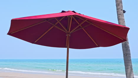 Low-angle-shot-of-a-red-parasol-on-a-clear-blue-sky-with-ocean-waves-reaching-the-shore