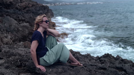 Woman-sitting-on-a-cliff-and-watching-the-surf-of-the-waves-breaking-on-the-rock