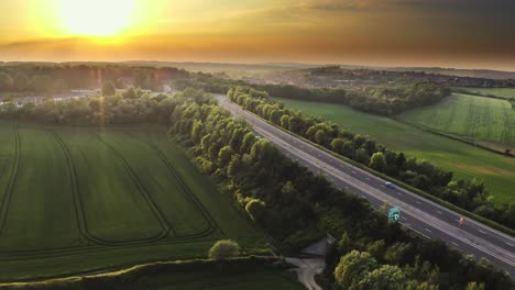 Aerial-view-over-a-highway-surrounded-by-green-fields-during-the-sunset-in-the-UK