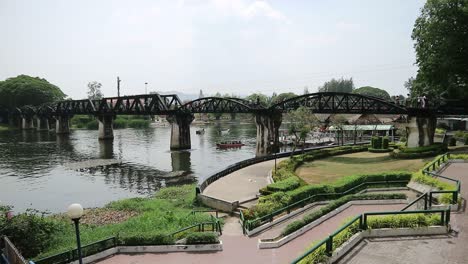 HD-Wide-Shot-of-Bridge-over-the-River-Kwai-in-Kanchanaburi,-Thailand-with-boats-under-the-historical-structure