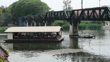 HD-Ferry-with-Tourists-Travelling-Under-the-River-Kwai-Bridge-in-Kanchanaburi,-Thailand