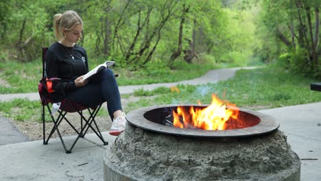 Beautiful-Brunette-Woman-Sitting-And-Reading-Book-By-The-Campfire-At-Daytime-In-American-Fork-Canyon,-Utah