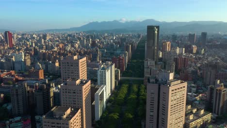 Aerial-flyover-Taipei-Cityscape-during-sunset-with-mountains-in-background