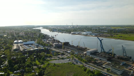 Shipyard-in-Poland-with-cranes-on-shore-of-Martwa-Wisla-river,-aerial