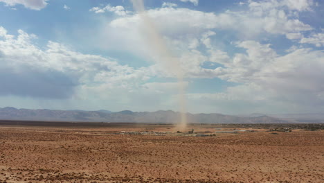A-sandstorm-or-dust-devil-with-spinning-wind-send-a-dust-cloud-in-the-sky-like-a-small-tornado---aerial-pull-back-view