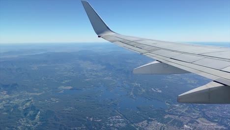 View-from-an-airplane-cruising-over-the-state-of-Queensland-in-Australia,-with-rainforests-and-large-lakes,-distant-hills,-blue-sky-and-a-hazy-horizon
