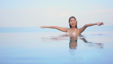 A-beautiful-young-woman-raises-her-arms-from-the-swimming-pool-waters-to-the-sky-in-joy