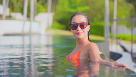 Face-close-up-of-Young-Asian-Woman-in-Her-30th-Inside-the-Water-Leaning-on-the-Border-of-the-Infinity-Pool-and-Turning-Sight-Into-the-Camera-with-Smile