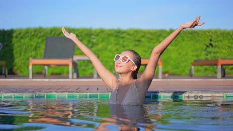 A-young-woman-in-a-swimming-pool-raises-her-arms-in-happiness