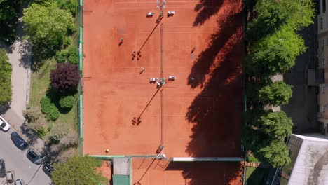 Aerial:-top-down-view-of-clay-tennis-courts,-people-playing-and-sweeping-courts