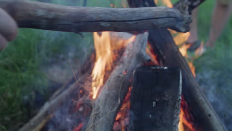 Guy-Person-Man-adding-firewood-logs-to-Campfire-Fire-Burning-in-Dusk-Evening-Night-in-Slow-Motion