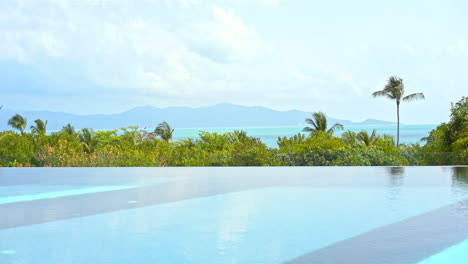 The-edge-of-a-resort-infinity-pool-overlooks-the-ocean-and-the-mountains-in-the-distance