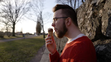 Eating-ice-cream-cone-Caucasian-European-man-sitting-on-bench-tasting-cold-frozen-delicious-dessert-sugar-sweet-vanilla-chocolate-fudge-summer-enjoy-sun-hot-warm-weather-biting-happy-satisfied-Swedish