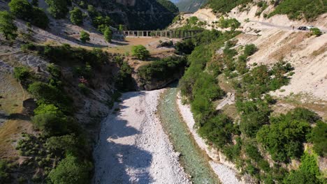 Pristine-river-branch-of-Vjosa-flowing-through-cliffs,-old-aqueduct-built-on-riverbanks,-Albania