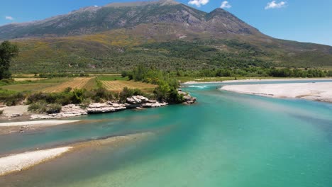 Rocky-banks-of-Vjosa-river-with-emerald-water-flowing-through-green-landscape-in-Albania