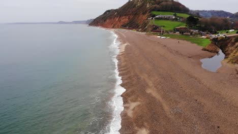 4K-Smooth-Aerial-shot-skirting-above-the-oceans-edge-and-glimpsing-the-mountains-and-rolling-hills-of-Branscombe-Beach