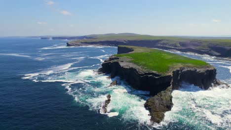 Aerial-hover-behind-Illaunonearaun-islet-with-Kilkee-cliffs-in-the-background-and-splashing-ocean-waves