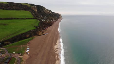 Amazing-4K-Aerial-shot-flying-above-the-oceans-edge-and-glimpsing-the-mountains,-rolling-hills-and-waves-of-Branscombe-Beach