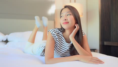 Portrait-of-beautiful-daydreamer-Asian-woman-lying-on-bed-thinking-and-smiling