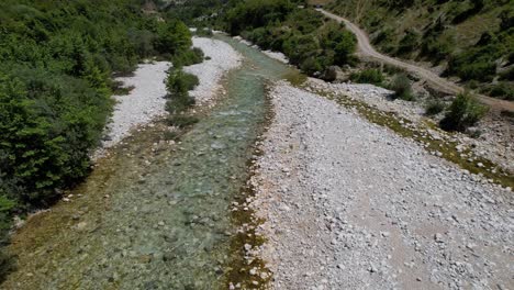 Flying-over-mountain-creek-with-cold-clean-water-surrounded-by-green-trees,-Vjosa-river-branch-in-Albania